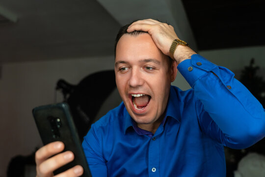 Surprised attractive man using internet on his mobile phone looking excited and shocked pulling hair. Funny businessman browsing telephone screaming in astonishment