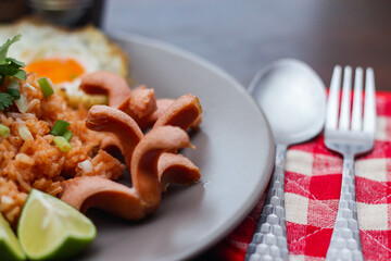 American fried rice served with fried sausage, cucumber, chopped vegetables in a gray plate on a brown wooden table with condiments.