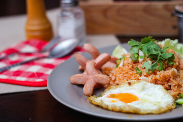 American fried rice served with fried sausage, cucumber, chopped vegetables in a gray plate on a brown wooden table with condiments.
