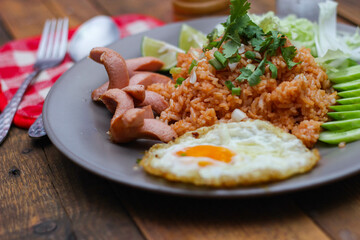 American fried rice is served with sausages, cucumbers, shredded vegetables in a gray plate on a slatted table with seasonings.