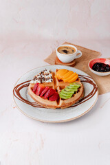 top view of waffles with peach, strawberries, ice cream, coffee on pink table