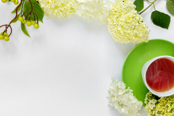 Сup of hot tea with bouquet of hydrangea on white background.