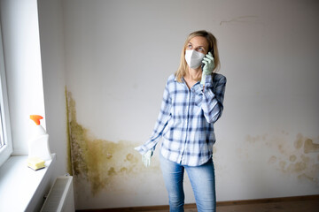 woman standing in front of wall with mold and talking on cell phone and is depressed and frustrated