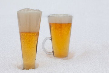 Two glasses of light beer with foam in the snow. Cold beer during winter.
