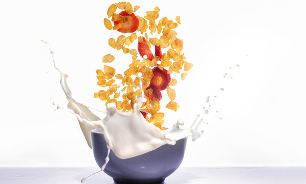 Corn flakes with strawberries falling and splashing into a bowl with milk