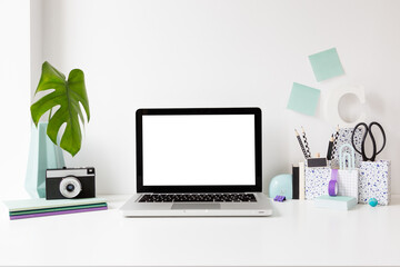 Office creative desk with white laptop screen, books and camera. Front view.