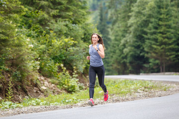 Obraz premium Runner woman running on the mountain road through the forest. Female sport girl training outdoors for marathon