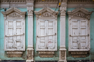 Three windows with closed shutters of an old house with carved decor and stucco, a fragment of the...