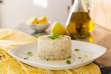 Vegan tofu cheese with parsley on a white plate. Extra virgin olive oil and lemons in the background. Vegan recipe