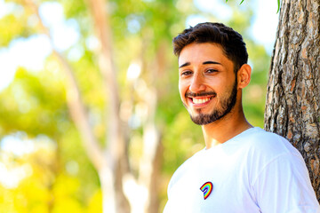 Handsome man in white shirt with rainbow badge outdoors - obrazy, fototapety, plakaty