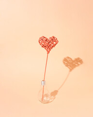 Knitted red heart in a light bulb on a pastel orange color. Minimal love flat lay.