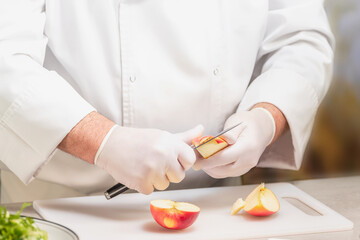 Unrecognizable chef in uniform cutting an apple on a plastic cutting board