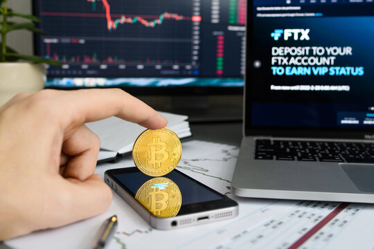 Vladimir, Russia - January 2022: Bitcoin coin on the background of computers with the FTX cryptocurrency exchange website. Selective focus on the coin.