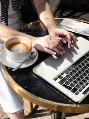 Fototapeta na wymiar Work life balance. A woman works on a laptop in a cozy cafe with a cup of coffee and an eclair in the morning sun.