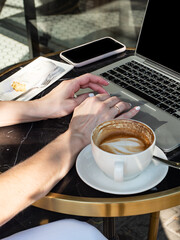 Work life balance. A woman works on a laptop in a cozy cafe with a cup of coffee and an eclair in the morning sun.