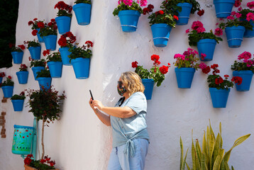 blonde woman on the street talking on the phone in andalusian village (spain) with flower pots hanging in the street