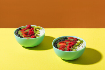 smoothie bowl with fresh berries and fruits in blue plate on yellow dark shadow