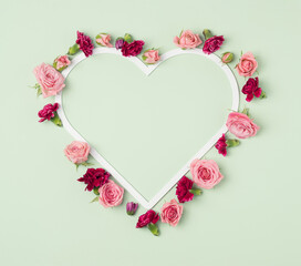 Heart frame with colorful flowers around it on a pastel green background. Valentine's mother's day backdrop