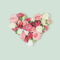 Colorful pastel flowers arranged in a heart shape on a pastel green background. Romance, love minimal concept.