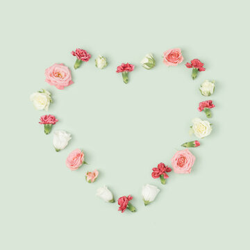 Various colorful spring flowers heart layout on a light green background. Valentine's day minimal concept.