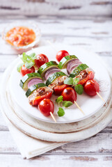 Grilled shashliks with vegetables and pork tenderloin. Bright wooden background. Close up.