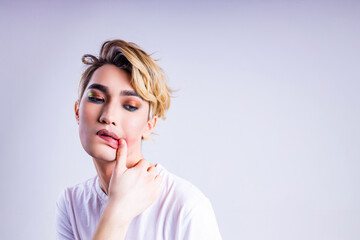 Closeup portrait of a young androgynous man smearing his lipstick ipstick over white background