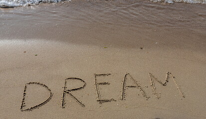 the inscription DREAM on the sand of the coastline