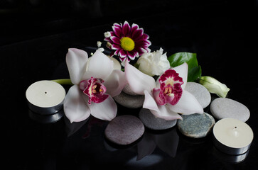 Obraz na płótnie Canvas Orchid flower with small flowers on gray stones with candles on a black background. spa composition
