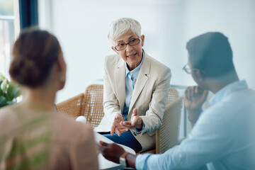 Mature insurance agent consults with couple while going through paperwork in the office.