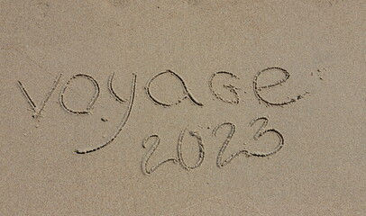 The inscription voyaje 2022 in French, travel 2022, on the sand by the water and the rising wave, seashore beach vacation by the sea