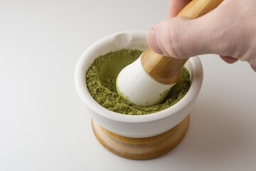 A man's hand grinds matcha tea in a mortar with a pestle. Preparation of Japanese matcha green tea.