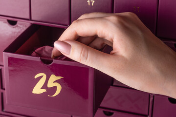 A woman's hand with a manicure opens the cell number 25 in the advent calendar. The girl takes out...