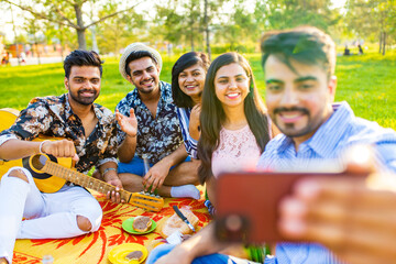 Best friends taking selfie outdoors while playing on guitar at picnic