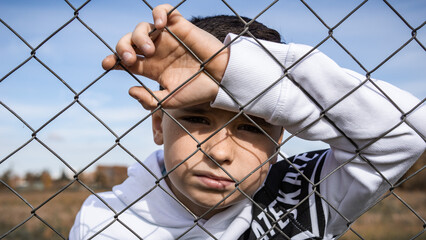 A young kid behind the fence posing his best and smiling and trying to be a model for one day