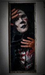 Vertical horrifying shot of a female in a mime costume posing behind a glass