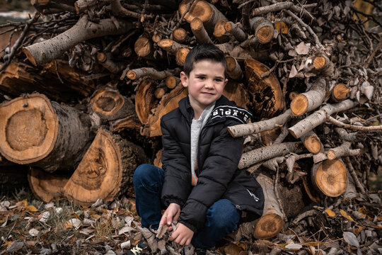 A young kid sitting on the logs and posing his best and smiling and trying to be a model for one day