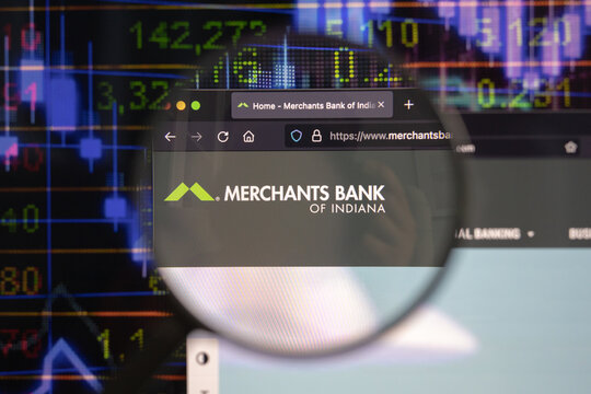 Merchants bank company logo on a website with blurry stock market developments in the background, seen on a computer screen through a magnifying glass.