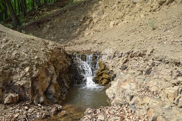 A small waterfall on clay soil on a spring day