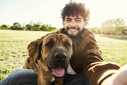 Young happy man taking selfie with his dog in a park - Smiling guy and puppy having fun together outdoor - Friendship and love between humans and animals concept