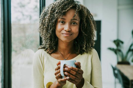 Portrait of young black woman holding cup of tea looking at camera - Close up face of happy hispanic girl at work - Confident businesswoman smiling in office - People lifestyle concept