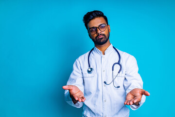 pakistanian doctor in white coat with stethoscope pointing at copyspace with hand mock up over blue studio background