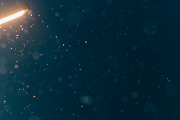 It is snowing and falling at night against the background of a night lamp on the street.