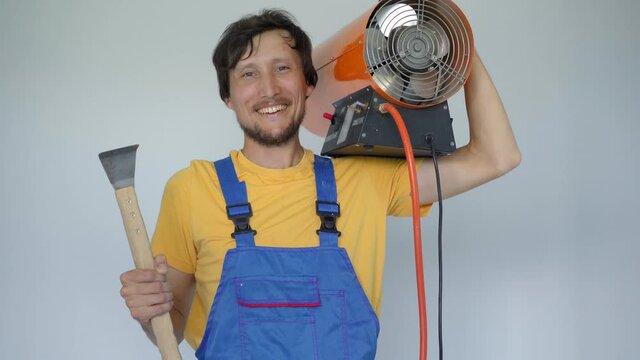 A Man Professional Home Renovator Holds A Propane Hot Air Heater And A Hook For Stretch Ceiling Installation In His Arms. He Looks At The Camera Smiling