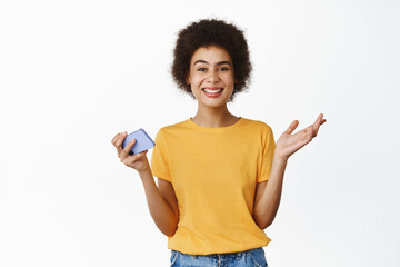 Portrait of attractive young modern african woman holding mobile phone, using smartphone app, standing over white background