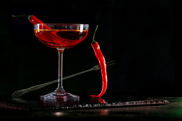 Cocktail with hot chilli pepper on bar counter in a restaurant, pub. Fresh spicy drink. Alcoholic cooler beverage on isolated black background
