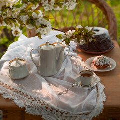 Coffee set on a white tablecloth on a sunny day, cherry blossom, cupcake, pudding. Outdoor, picnic, brunch, spring mood. Soft focus