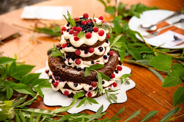 A wedding cake with red berries served outdoors. Cutlery in the background.