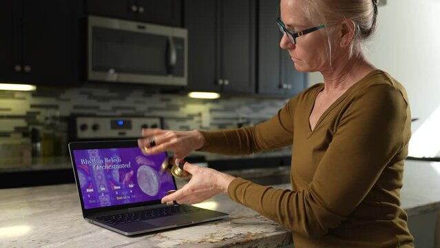Mature woman takes remote lesson to learn finger cymbals online on a laptop. Remote learning concept.