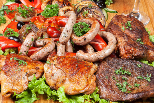 grilled meat closeup. chicken, pork, sausages and vegetables on the wooden board