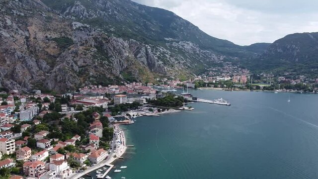 Smooth aerial of beautiful Kotor Old Town and marina bay shot with drone on summer day in Montenegro, view of historical architecture, tourist attractions, boats in harbor, people on beach park
